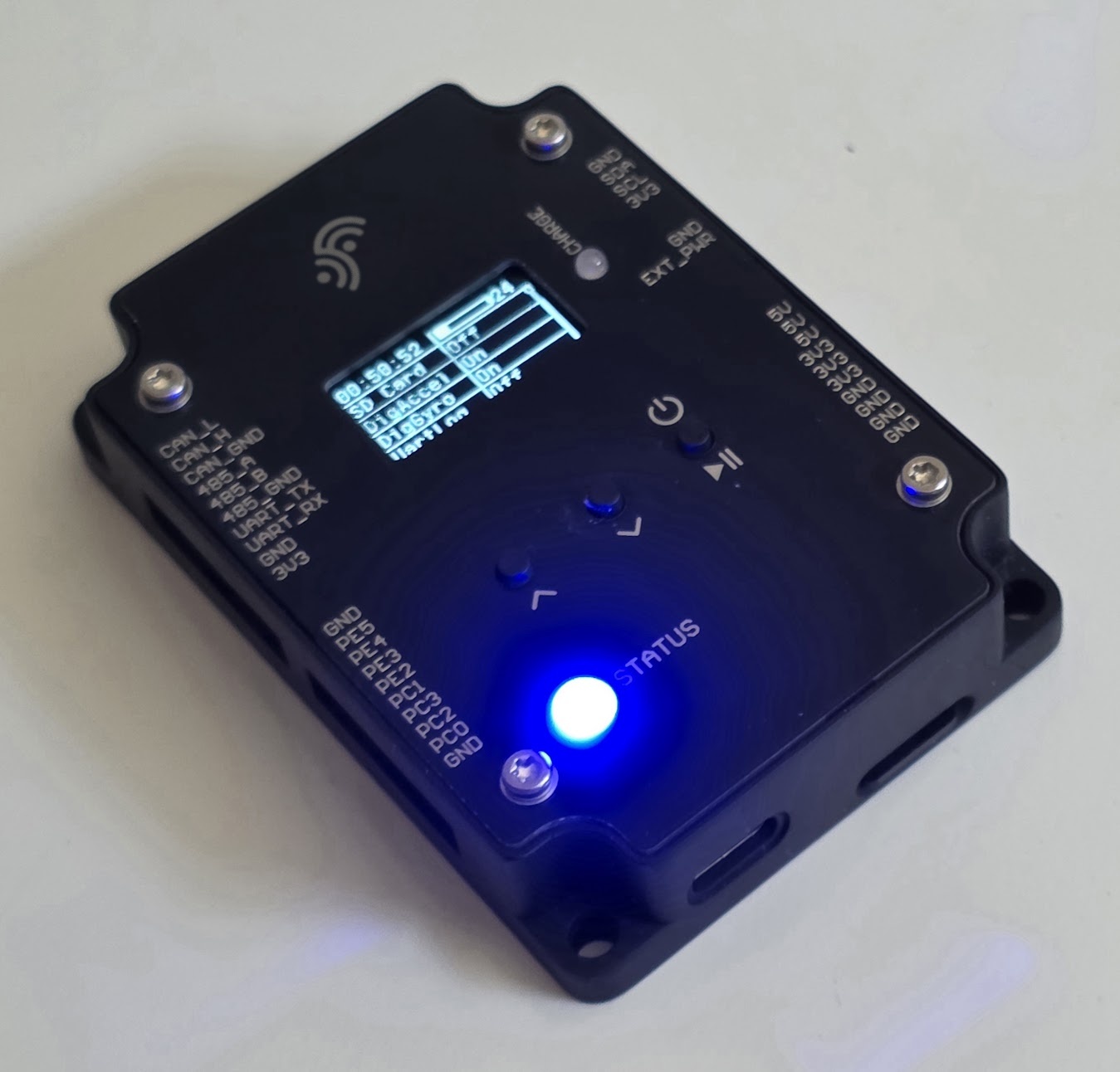 Fluxterra three-axis vibration logger prototype: black machined enclosure with OLED status display, illuminated status LED and silkscreened CAN, RS-485, UART and GPIO port labels.